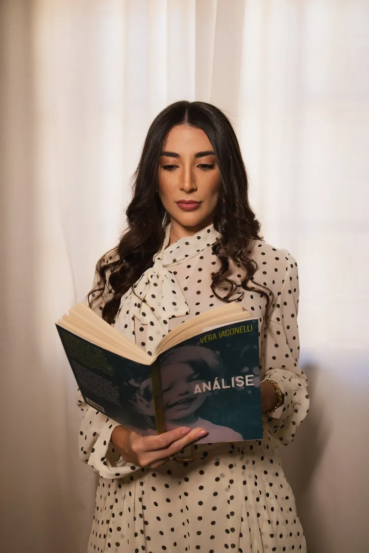 Jennifer lendo o livro Análise, de Vera Iaconelli, diante de uma cortina iluminada